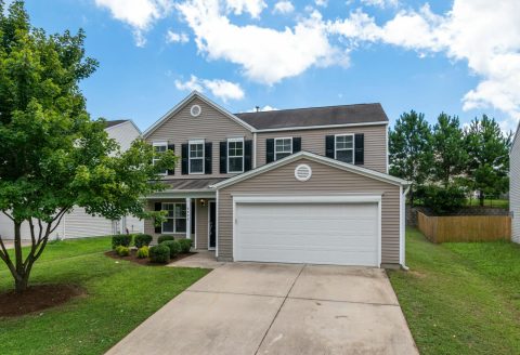 Charming two-story suburban home with green lawn, two-car garage, and blue sky.